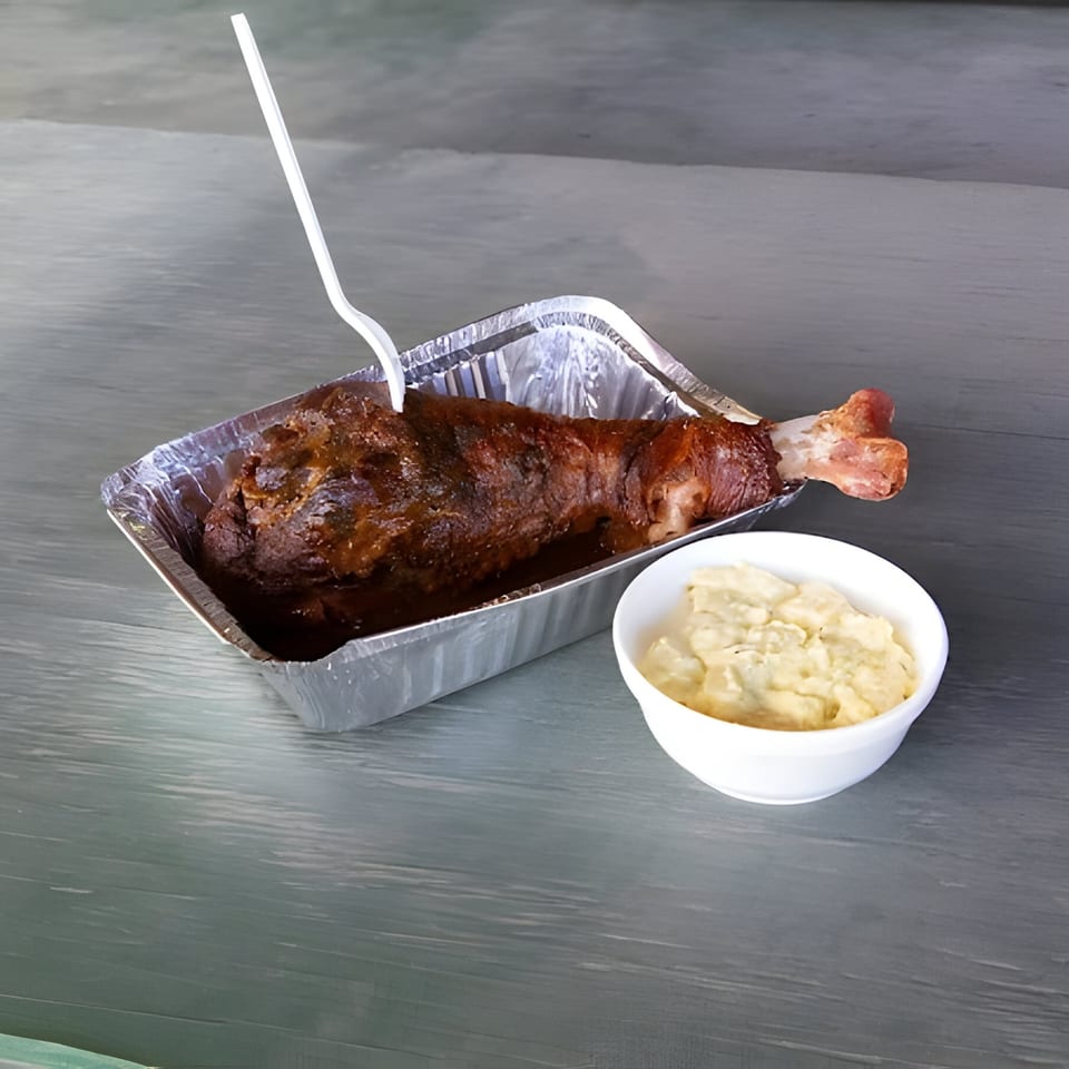 Mosito's BBQ turkey leg with a plastic fork in a foil pan, next to a side of mac and cheese.