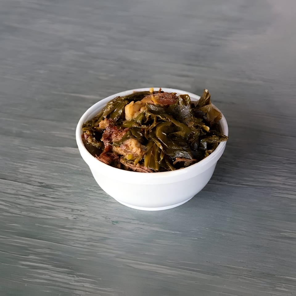 A white bowl filled with Mosito's BBQ collard greens and pieces of meat on a gray wooden surface.