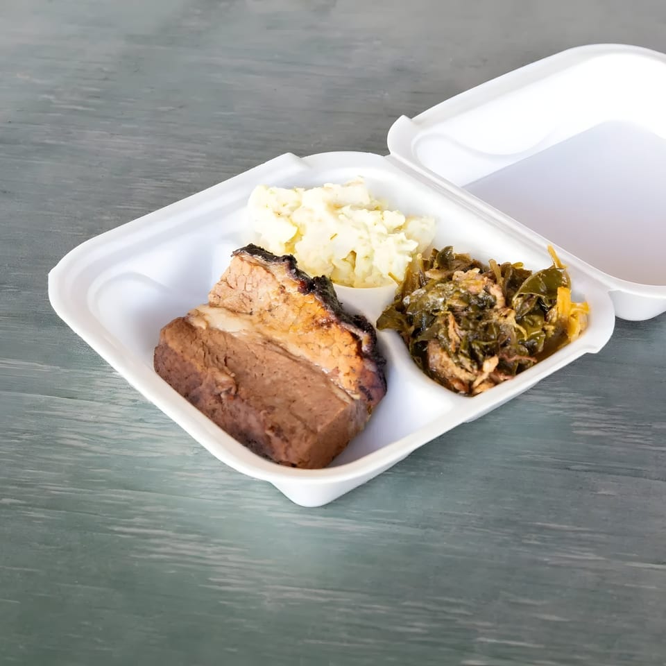 Mosito's BBQ brisket, mashed potatoes, and collard greens in a white takeout container.