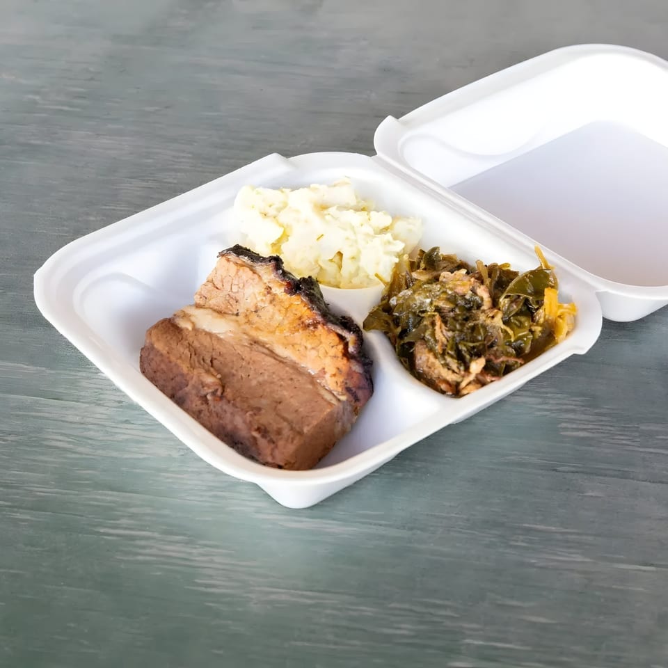 Mosito's BBQ brisket, potato salad, and collard greens in a white takeout container.