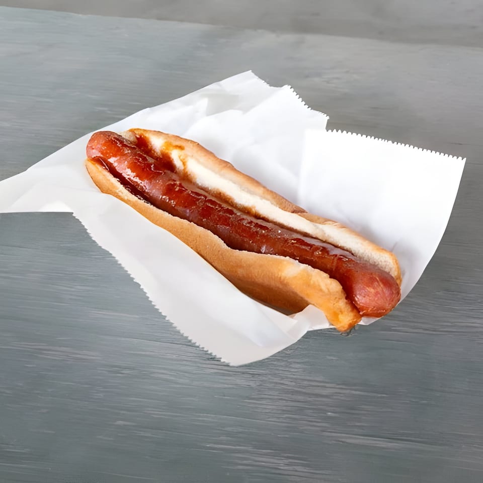 A Mosito's BBQ hot dog with ketchup in a white paper wrapper on a gray table.